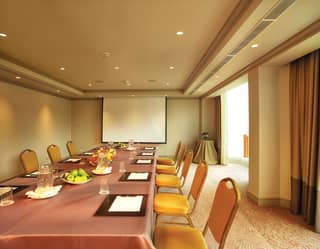 Long banquet table with orange chairs facing a flat screen in a meeting room