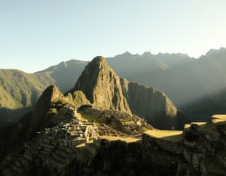 Sunshine illuminates the ancient ruins of Machu Picchu, cradled between the verdant peaks of Huchuy Picchu and Huayna Picchu.