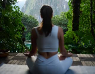 A guest sits in easy pose as she does yoga at the relaxation area, with incredible views of Machu Picchu, seen from behind.