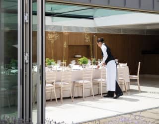 A waiter puts the finishing touches to a long table set for more than 16 diners on an outdoor terrace surrounded by lavender