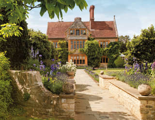 Stone path leading to a vast manor-house with manicured stone-walled gardens