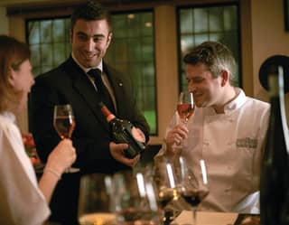Smiling sommelier showing a wine bottle to two smiling cookery students