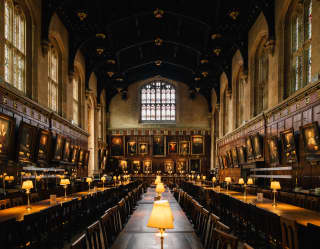 The dining hall of Christ Church College, Oxford. Portraits hang from wood panelled walls, lamps light rows of wooden tables