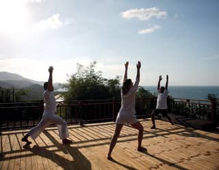 Guests enjoy a yoga session on wooden decking overlooking the ocean below