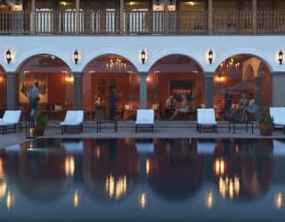 Hotel pool in evening light reflecting the lights of an arched cloister beyond
