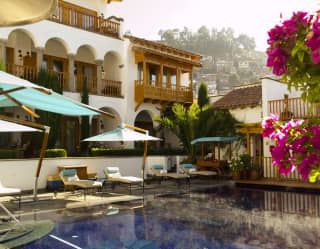 Outdoor hotel pool lined with sunbeds with trees and hotel in the background