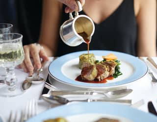 a steward is pouring a gravy over a guest's dish