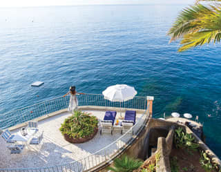 Lady gazing over a rail from a sun terrace on a cliffside overlooking the sea