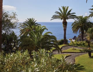 Cobbled paths meander through lush lawns and shrubs in the stunning botanical gardens, with palm tree pillars and sea views.