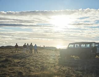 On the grassy top of Pico de Arieiro mountain, five guests stand by two jeeps, watching the sun rise above a bank of cloud.