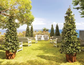 A corner of the exotic gardens overlooking the sea is ready for a memorable occasion with a wedding table and bench seating.