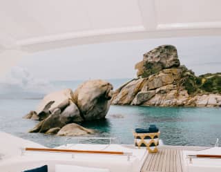 Incredible cream-hued granite rock formations rise from the luminous waters, seen from the covered deck of a leisure boat.