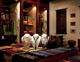 A gift shop with tables and shelves of traditional Laos fabrics, jewellery, vases and bowls, and richly woven wall hangings.