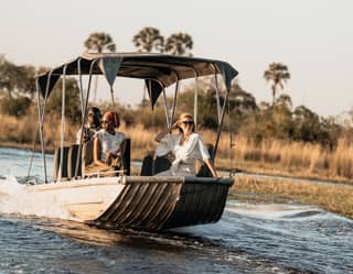 Stylish guests sitting at the bow of a motor boat sailing along a river among grasslands