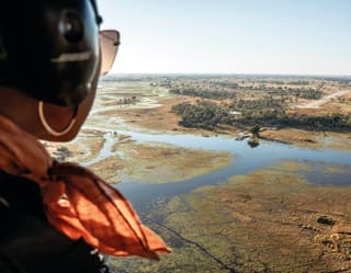 Lady with sunglasses and coral scarf gazing at the Okavango Delta from a helicopter