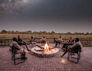 Group of guests sitting around a campfire gazing at a starry sky in the savannah