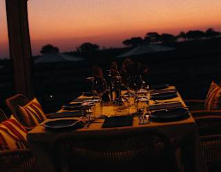A deep sunset paints the sky peach and purple, bathing a restaurant dining table with views in a glowing rose-gold light.