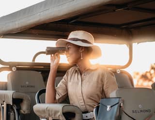 A female guest watches wildlife through binoculars from the comfort of her seat in the safari vehicle
