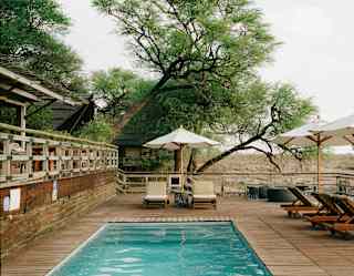 View from one end of the blue pool, bordered on two sides by lounge chairs and parasols and on the other by a raised terrace.