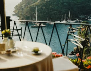 The vibrant blue of the gulf of Portfino dazzles beyond the railings of La Terrazza's terrace, viewed over a vacant table.