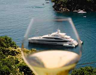 A yacht appears trapped in a drink of white wine in a shot of Baia Cannone, seen from above through a sauternes-shaped glass.