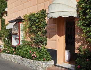 Entrance of a peach-coloured boutique, lined with pink rose flower beds