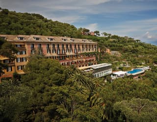 The pink walls and arched windows of the Hotel Splendido rise elegantly out of green canopy of trees that fill its gardens