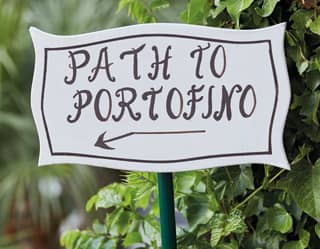 A charming hand painted black on white sign emerges from the greenery to declare 