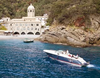 Motorboat sailing towards a bay with a medieval stone church on the shore