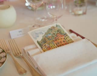 A watercolour postcard of Portofino's colourful houses is tucked into a table napkin. Posies of sweet peas fill glass vases