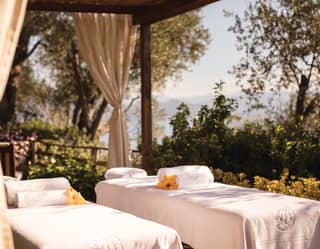 Twin treatment tables topped with fluffy white towels and large yellow hibiscus flowers enjoy dappled shade on the terrace