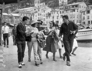 A group of young friends are walking quickly and talking animatedly on Portofino's harbour wall  in this black and white image