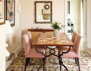Chairs upholstered in pale pink velvet sit at a table decorated with geometric marquetry. An door opens onto a sitting room
