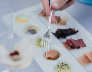 A man dips a slice of lattume into a sauce on a fish charcuterie tasting platter of six Trapani delicacies and Sicilian condiments
