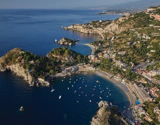 Aerial view of yachts bobbing in Taormina bay with residences coating the hills