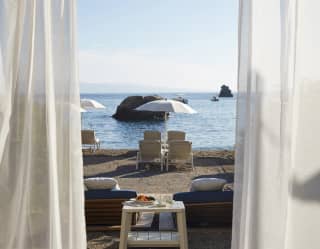 View through linen drapes of sunbeds under a white parasol on a shoreline