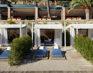 Row of luxurious beach cabanas lining a shore with blue sunbeds in front