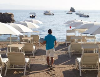 Beach steward strolling towards the sea between rows of sunbeds