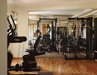 Looking into a light-filled gym with a polished wooden floor and a selection of exercise and resistance machines.