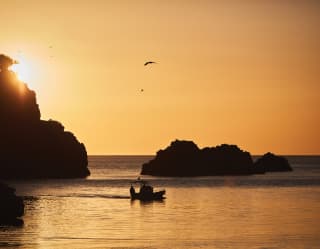 Silhouette of a sailing boat sailing in a rocky bay in an orange sunset