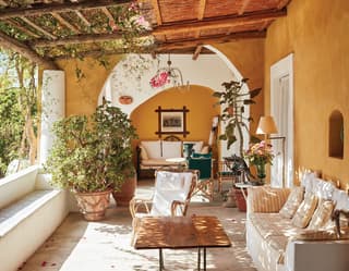 Dappled light filters through a cane and bougainvillea loggia roof. Pink petals dusting the floor like confetti among the sofas