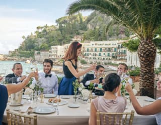 Guests at a formal wedding table on an outdoor terrace overlooking Taormina