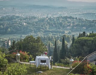 A table for two occupies a secluded corner of the garden. Cypresses reach to the sky as the hillside falls down to Florence