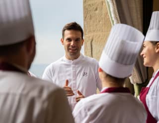 In a sunny window at La Loggia restaurant, Chef Alessandro Cozzolino talks to staff, who wear red aprons and white toques.