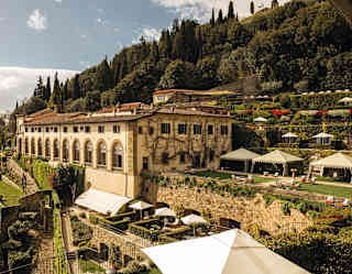 A high-angle view over Villa San Michele nestled between steep garden terraces with parasols, gazebos and manicured features.