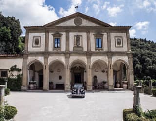 A vintage car is parked outside the Michelangelo-designed facade of the Belmond Villa San Michele. Lush hill touch the sky