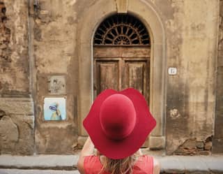 Lady in a red wide-brimmed hat taking a photograph of an old Florentine street