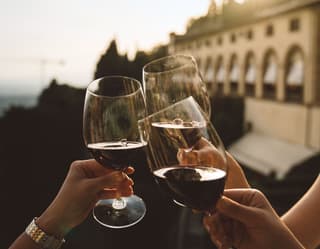 Three glasses full of red wine clinking together in a toast