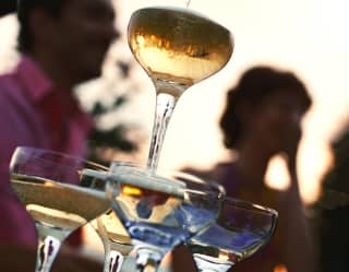 Sun plays in a full coupe glass atop a pyramid as Champagne continues to pour, cascading into four below, seen from beneath.