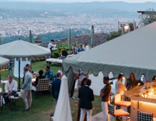 Guests of a special event sit at tables and mingle by the outside bar in the gardens, with sweeping views over Florence.